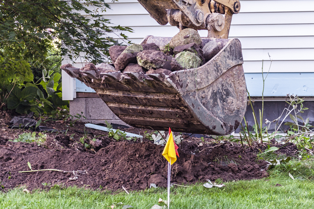 Large excavator digging up a lawn due to an emergency plumbing service.