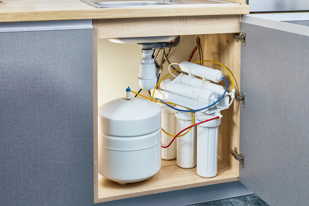 A new water filtration system under kitchen sink with yellow, red and blue cords.
