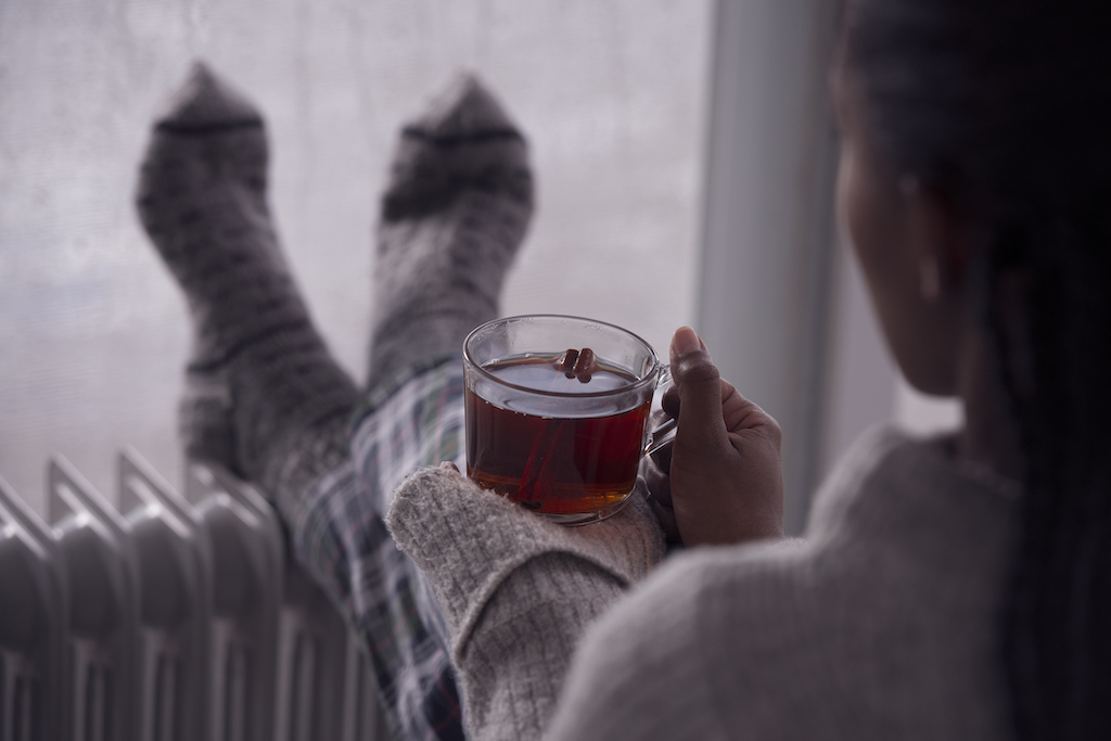 Woman cozy by her heater drinking warm tea and fuzzy socks, thanks to water heater repair.