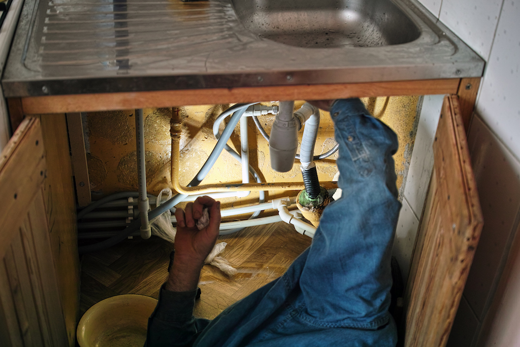 Person fixing leak under sink. Commercial plumbing services.