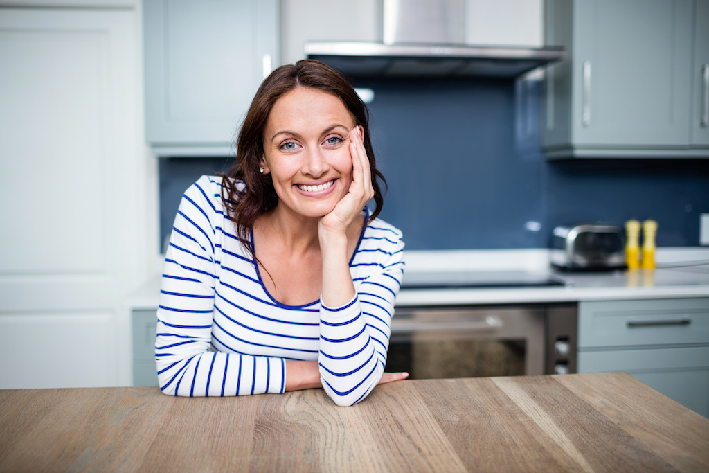 Happy woman smiling into camera in her kitchen. | garbage disposal repair and installation