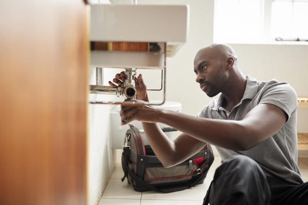 Plumbing Problems, male plumber sitting on the floor fixing a bathroom sink.